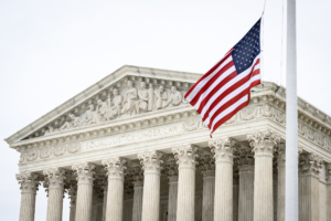 Front view of the U.S. Supreme Court building with an American flag waving in the foreground, symbolizing justice, law, and patriotism.