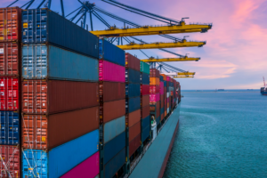 A large cargo ship docked at a port being loaded with colorful shipping containers under cranes, illustrating global trade and Incoterms-related logistics and insurance responsibilities.