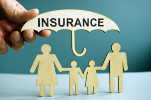 Wooden family figures under an umbrella labeled “Insurance,” representing protection from umbrella insurance coverage gaps.