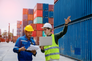 Two logistics professionals reviewing supply chain documentation at shipping container port discussing coverage gaps and insurance protection needs