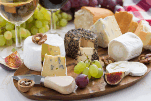 Artisanal cheese board with premium imported cheeses, fresh grapes, figs, and wine glass displaying high-value specialty food products requiring specialized insurance coverage
