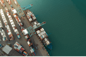Aerial view of container ship at port terminal showing multi-modal food transport infrastructure with shipping containers and cranes